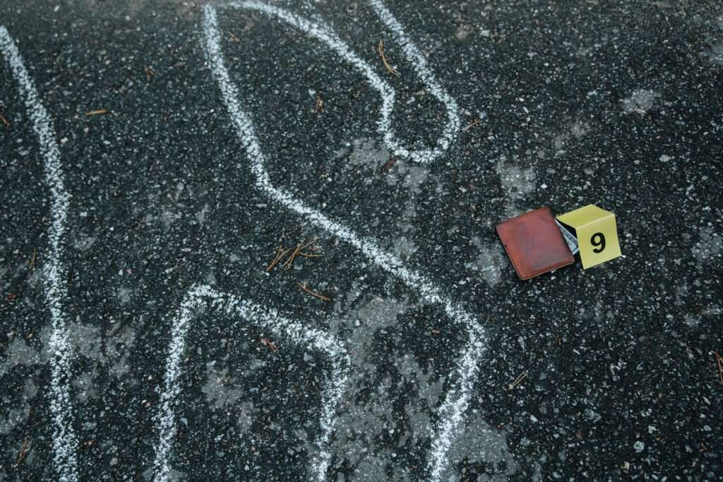 Crime scene with a chalk outline and evidence marker on asphalt.